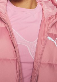 Miękka różowa kurtka o gładkiej, błyszczącej fakturze, z białym logo. Nałożona na różową koszulkę z krótkim rękawem z delikatnym wzorem.