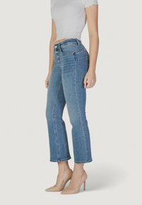 Vaqueros cortos de color azul claro con cierre de cinco botones, pierna recta, dobladillo sin terminar y textura clásica de denim, combinados con tacones altos nude.