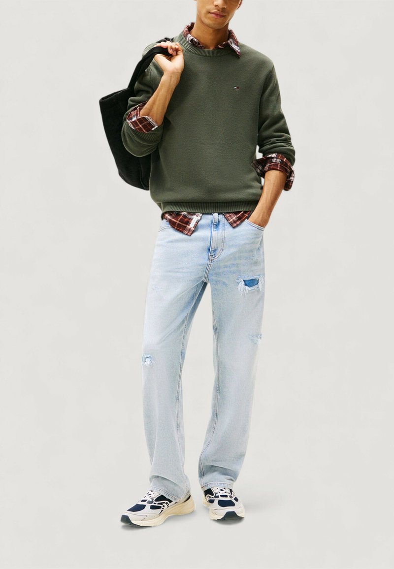 Maglione verde, camicia a quadri sotto, jeans azzurri strappati, borsa tote nera e sneakers blu navy con dettagli bianchi. Design di un outfit casual.