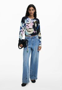 Long-sleeve, navy floral sweater with pink, blue, and white patterns, paired with light-wash wide-leg jeans and a black handbag with a charm.