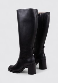 Botas de cuero negras hasta la rodilla con punta redonda, tacón cuadrado y cremallera trasera. Presentan pequeños detalles cerca del tobillo para un toque adicional.