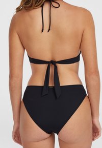 Čierny bikiny set s topom na zaväzovanie za krkom a vysokými nohavičkami. Hladká látka, žiadne vzory, minimálne kovové akcenty.