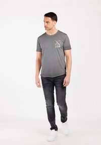 Camiseta gris de manga corta con un gráfico floral en el pecho, combinada con jeans de mezclilla oscura y zapatillas blancas.