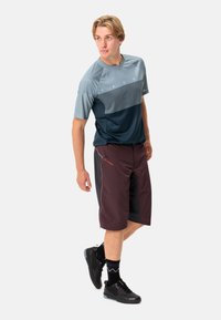 Completo atletico maschile con una maglietta color blocco grigia e blu navy e pantaloni corti bordeaux, realizzati in materiale leggero e traspirante. Sneakers nere.