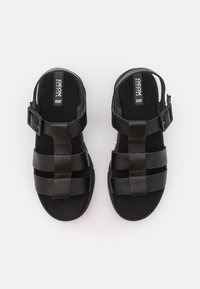 Černé sandály se třemi vodorovnými pásky, s přezkou kolem kotníku a texturovanou stélkou pro pohodlí.