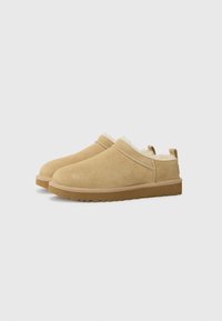 Scarpe slip-on in suede beige con una morbida fodera bianca, punta rotonda e suole in gomma con grip testurizzato. Piccolo tallone posteriore per aiuto nell'indossarle.