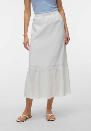 Femme portant une jupe blanche jusqu'aux chevilles avec un ourlet à volants, un top sans manches bleu clair et des sandales crème à brides tressées.