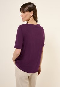 T-shirt viola a maniche corte con scollatura rotonda, realizzato in tessuto leggero, caratterizzato da una vestibilità morbida e maniche arrotolate. Vista posteriore semplice.