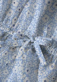 Vestido de tela azul claro con estampado floral, que presenta flores blancas y azul oscuro. Incluye una cintura elástica con un detalle de lazo a juego.