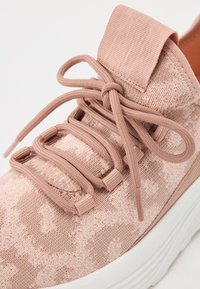 Różowy but sportowy z teksturowaną tkaniną na cholewce, elastycznymi sznurowadłami i pętelką do zakładania; posiada białą, amortyzowaną podeszwę i subtelny wzór.