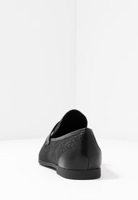 Scarpa nera slip-on con parte superiore in tessuto testurizzato e dettagli in pelle liscia. Presenta un tacco basso e una punta arrotondata per un design informale.