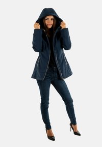 Giacca impermeabile blu navy con cappuccio, chiusura frontale con zip e tasche laterali, design aderente e texture del tessuto liscia e lucida.