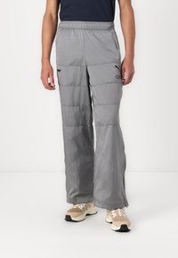 Grå polstrede bukser med elastisk talje, der har sidelommer med lynlås og en let, glat tekstur, parret med beige sneakers.