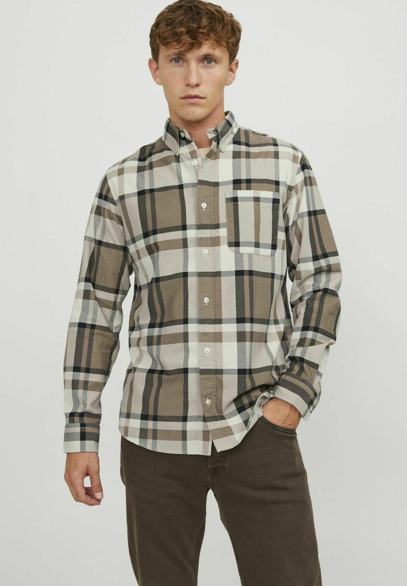 Camisa de botones hecha de tela tejida en un patrón de cuadros beige, marrón y negro; cuenta con un collar y un bolsillo en el pecho.