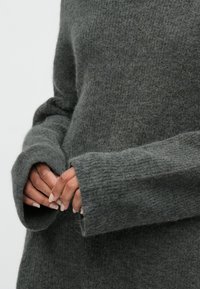 Harmaa, teksturoitu neulepusero, jossa on leveät hihat ja väljä istuvuus. Karkea, pörröinen materiaali, jossa on näkyviä kuituja ja ribbed hihansuut.