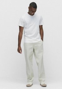 Hvid kortærmet t-shirt med en subtil tekstur, parret med lysebeige løstsiddende bukser og cremede sneakers. Minimalistisk design.