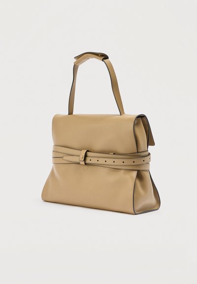 Sac à main en cuir fauve avec un large rabat et un détail de ceinture ajustable, doté d'une seule sangle supérieure et de coutures bordées de noir sur un fond blanc.