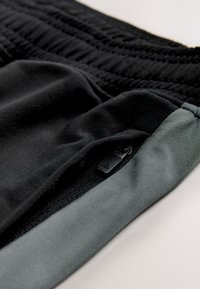 Fekete sportos rövidnadrág texturált derékpántekkel, cipzáras zsebbel, fekete húzófüllel és világosszürke szegéllyel.