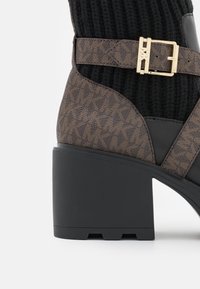 Bottine marron à motif avec talon noir épais, bride à boucle dorée et tige en tissu côtelé noir.