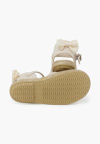 Lichtbeige sandalen met een bovenwerk van stof, een strikaccent op de enkelriem en een gestructureerde rubberen zool. Maat- en productiedetails zichtbaar.