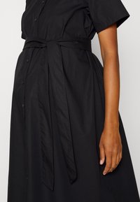 Vestido preto de algodão com mangas curtas, frente com botões e um cinto de tecido atado na cintura. Apresenta uma textura suave e um design versátil.