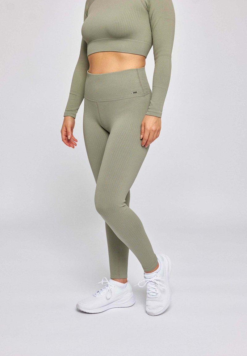 Ensemble de vêtements de sport vert à côtes comprenant un crop top à manches longues et un legging taille haute, associé à des chaussures de sport blanches.