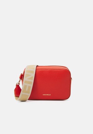 Lille rektangulær rød læder crossbody taske med beige justerbar rem og gyldent metal lynlås, mærket COCCINELLE foran.