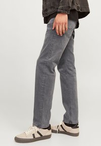 Gray denim jeans with a straight fit, subtle texture, and stitched back pockets, paired with beige sneakers featuring black stripes.