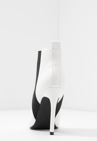 Botín blanco y negro hasta el tobillo con puntera puntiaguda, tacón de aguja y paneles laterales elásticos. Combinación de cuero suave y tejido texturizado.