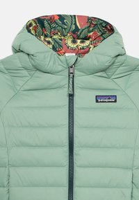 Zelená pufrová bunda so zipsovým uzáverom, ktorá má farebne vzorovanú podšívku a horizontálne prešívanie pre lepšiu izoláciu. Logo Patagonia na hrudi.