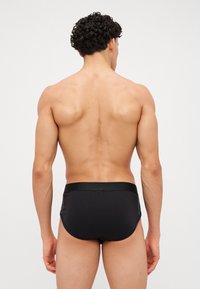 Schwarze Schwimmshorts mit glattem Material und elastischem Bund, die ein figurbetontes Design und minimale Abdeckung aus der Rückansicht zeigen.