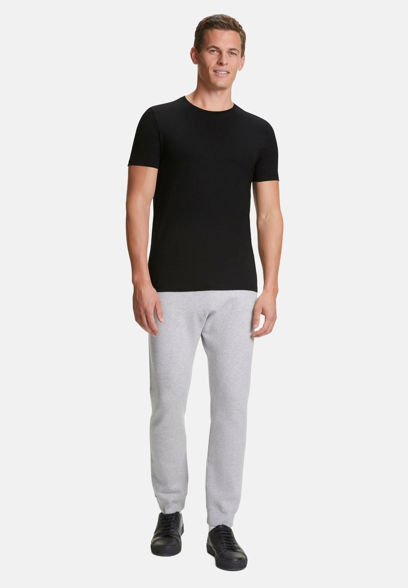 Zwarte korte mouwen t-shirt gecombineerd met lichtgrijze sweatpants en zwarte sport schoenen. Eenvoudig ontwerp, aansluitende vorm en katoenachtige textuur.