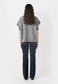 Grå stickad poncho med lös passform, korta ärmar och ribbat avslut, i kombination med mörkblå utsvängda jeans med en klassisk femfickdesign.