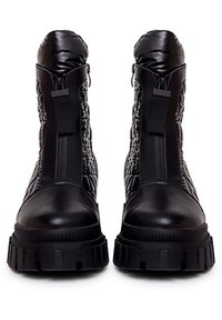 Botines negros hasta el tobillo con parte superior de nailon acolchado, detalles en cuero liso, cremallera frontal y suela gruesa de goma. Acentos texturizados en negro.