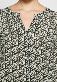 Chemise à motifs avec un décolleté en V, fabriquée en tissu léger avec un imprimé géométrique noir, blanc et vert menthe.