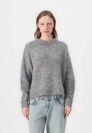 Grå, lodden genser med rund hals, lange ermer og en litt cropped hem. Båret over lyseblå denimjeans.