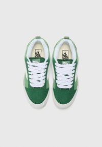 Green sneakers with a suede upper, white laces, and rubber soles. Features a padded collar and Vans logo on the tongue.