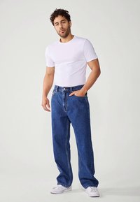 Hvit T-skjorte med korte ermer kombinert med løstsittende blå denimjeans. Jeansene har en klassisk fem-lommes design og rette ben.