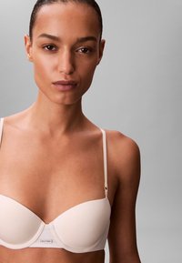 Reggiseno nude liscio Calvin Klein con coppe sagomate, spalline regolabili e sottili dettagli in oro. Tessuto morbido con design senza cuciture.