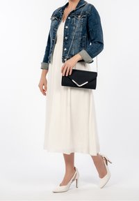 Pochette noire avec un accent argenté, veste en jean avec détails à boutons, robe blanche, et chaussures à talons crème avec design ajouré.