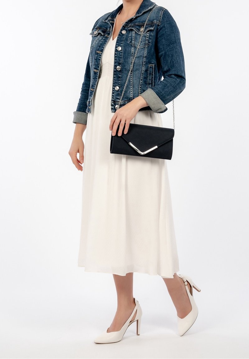 Pochette noire avec un accent argenté, veste en jean avec détails à boutons, robe blanche, et chaussures à talons crème avec design ajouré.
