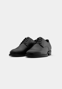 Chaussures noires en cuir à lacets avec un bout arrondi, une semelle plate et un design minimaliste. Texture lisse avec des détails de couture subtils.