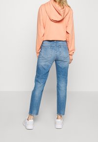 Jeans de denim azul claro con un corte relajado, cintura alta y dos bolsillos traseros, combinados con un sudadera con capucha de color melocotón.