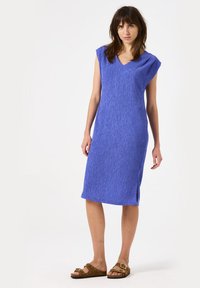 Vestido azul hasta la rodilla con mangas cortas, escote en V, tejido texturizado y aberturas laterales. Combinado con sandalias marrones con hebillas.