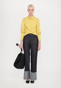 Gul skjorte med lange ermer, kombinert med mørk denim vide bukser med grå mansjetter. Svart vevd håndveske, svarte leiligheter.