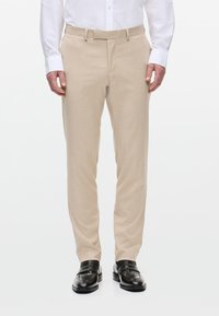 Pantaloni beige su misura con una texture liscia, passanti per cintura e davanti piatto, abbinati a mocassini neri lucidi. Design casual formale.