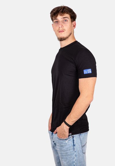T-shirt nera a maniche corte con scollo rotondo e etichetta blu "ICON" sulla manica sinistra, abbinata a jeans azzurri.