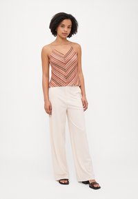 Strappy top, jossa on vaaleanpunainen, beige ja ruskea sahalaitakuosi. Yhdistetty vaaleanbeigeihin leveisiin housuihin ja mustiin liukuviin sandaaleihin.