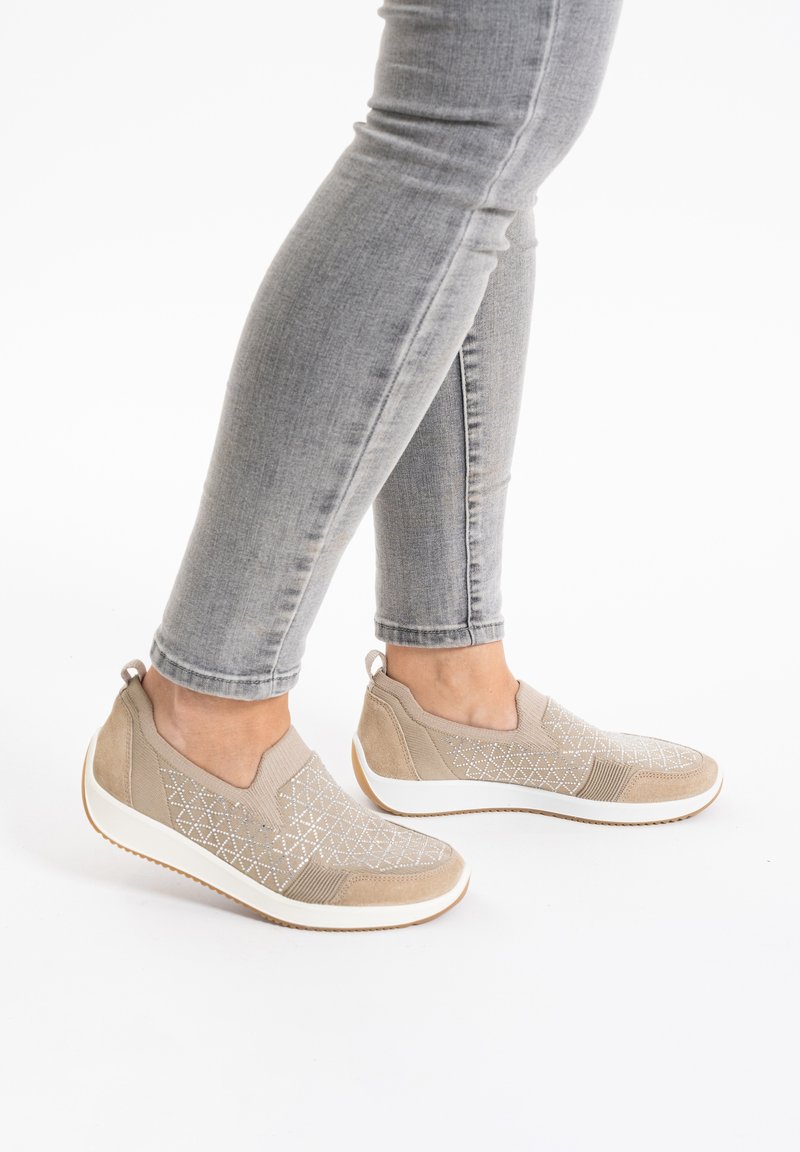 Beige nazouvací boty s texturovaným textilním svrškem s diamantovým vzorem a bílou gumovou podrážkou, doplněné o těsně padnoucí šedé džíny.