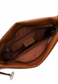 Interno di una borsa a mano in pelle marrone con una finitura texture. Include una tasca con cerniera, fodera liscia e un piccolo tag del marchio. Chiusura con cerniera nella parte superiore.